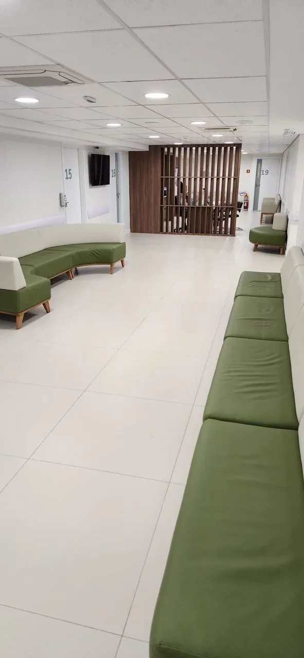 Corredor de espera do Pilar Centro Médico, claro, com sofás de estofado verde-musgo e divisória de ripas de madeira ao fundo